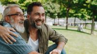 Two men smiling and sitting together in a park.